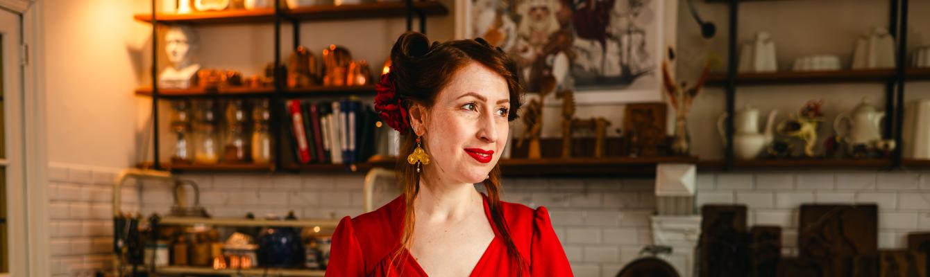 Een vrouw in een rood kleed poseert in een keuken.