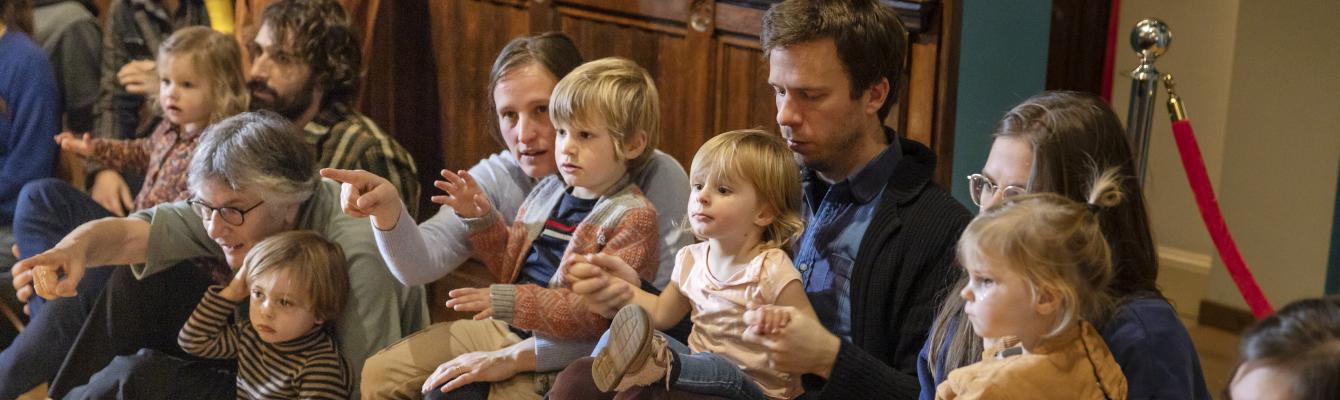 Ouders en kleine kinderen zitten in een museumzaal.