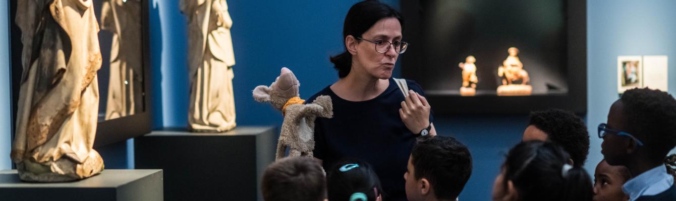 Een vrouw leidt kinderen rond in een museumzaal.