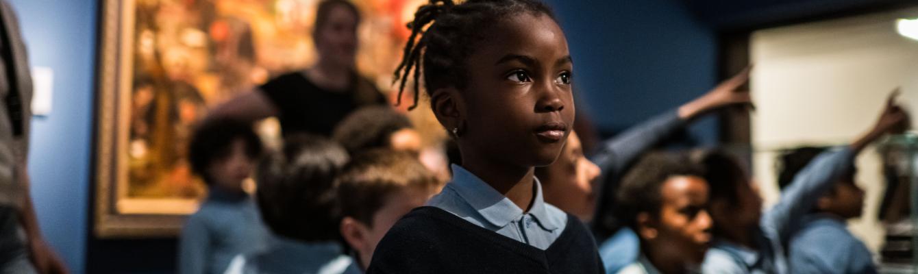 Enkele kleine kinderen kijken in een zaal met schilderijen voor zich uit.
