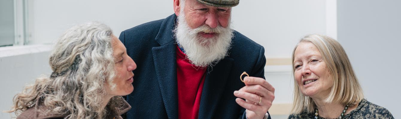 Een man houdt een ring met puntdiamant vast. Twee vrouwen die naast hem staan, kijken vol bewondering toe.