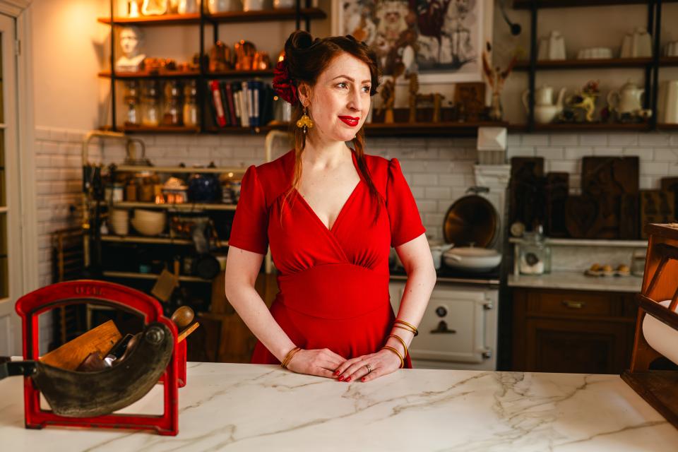 Een vrouw in een rood kleed poseert in een keuken.