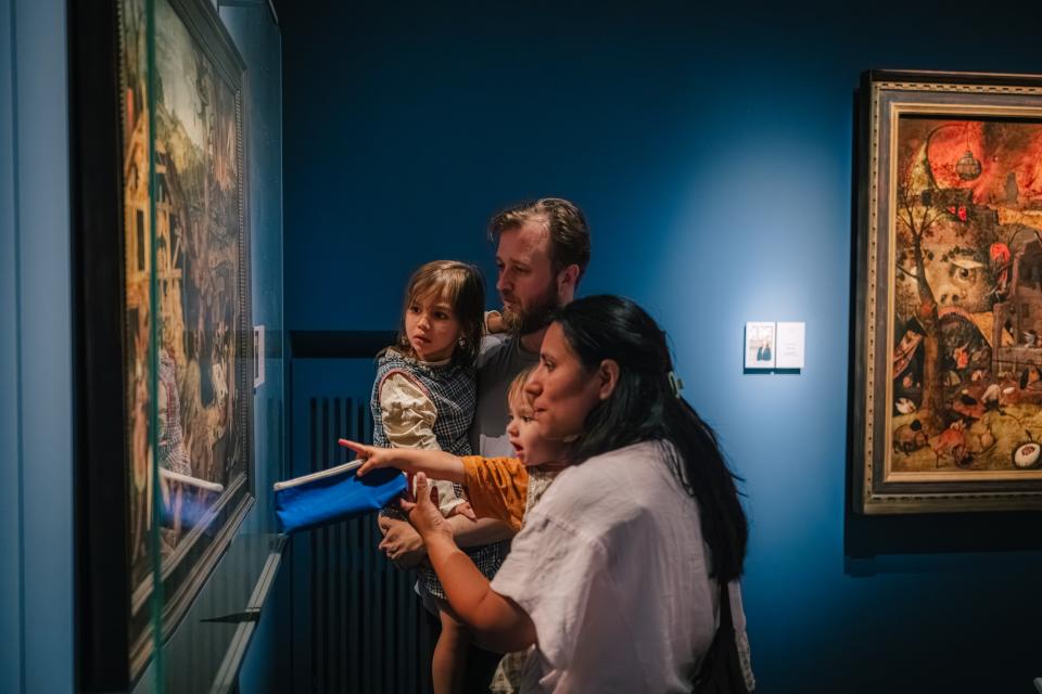 Een vader, moeder en twee kleine kinderen kijken naar een schilderij van Pieter Brueghel.