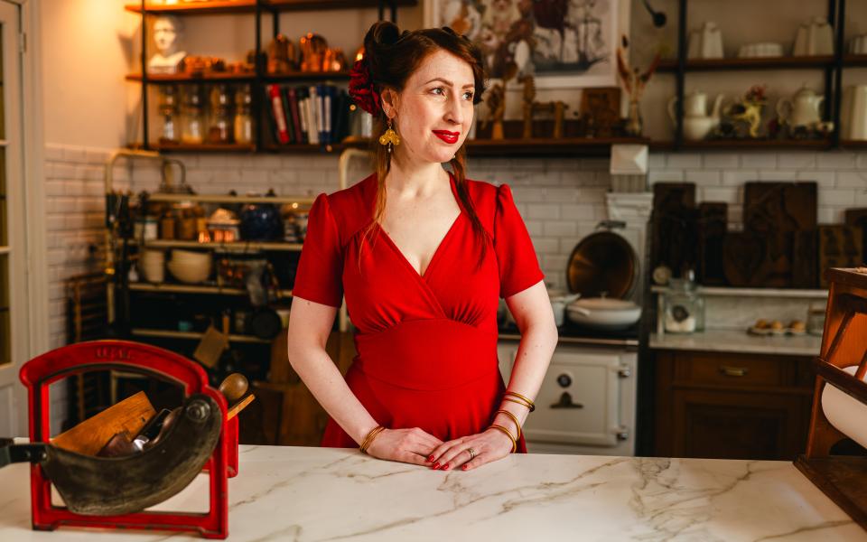 Een vrouw in een rood kleed poseert in een keuken.
