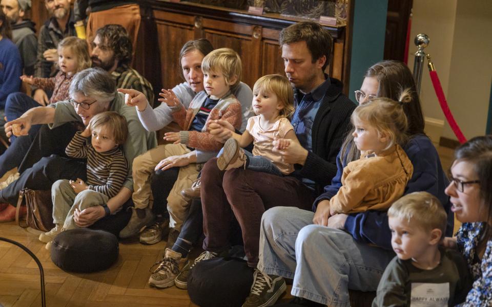 Ouders en kleine kinderen zitten in een museumzaal.