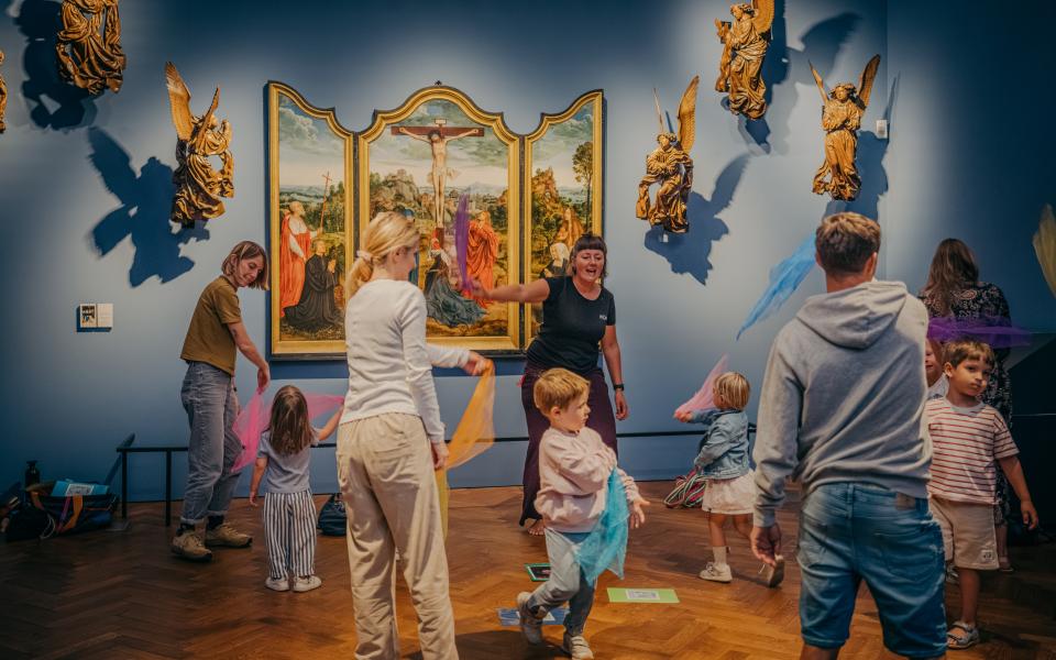 Kinderen en volwassenen gooien met slingers in een museumzaal.