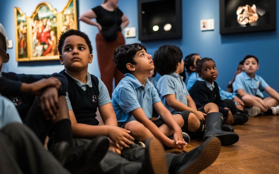Een groep kinderen uit het eerste leerjaar zit op de grond en kijkt naar de kunstwerken.