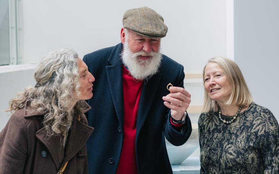 Een man houdt een ring met puntdiamant vast. Twee vrouwen die naast hem staan, kijken vol bewondering toe.