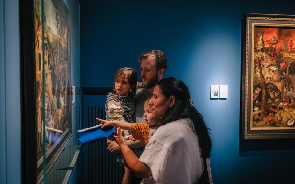 Een vader, moeder en twee kleine kinderen kijken naar een schilderij van Pieter Brueghel.