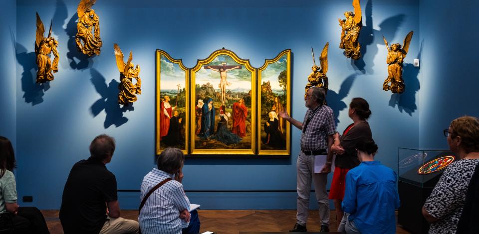 Een groep mensen kijkt naar het drieluik Calvarie met stichterspaar