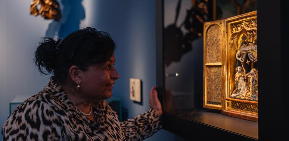 Een vrouw kijkt naar een altaarstuk in een museumzaal.