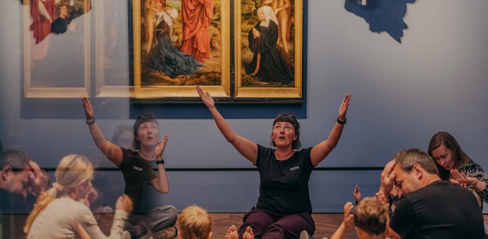 Kinderen en een paar volwassenen zitten in een museumzaal.