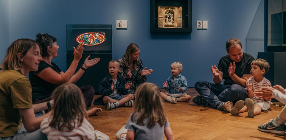 Kinderen en hun ouders zitten in een museumzaal.